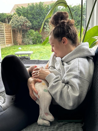 Victoria breastfeeds her baby on her sofa at home.