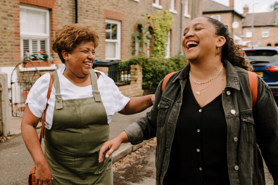 Two women walking down a residential street, laughing.