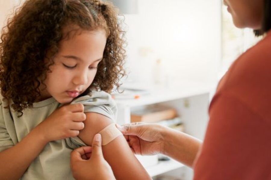 Young girl looking at plaster on arm after vaccination