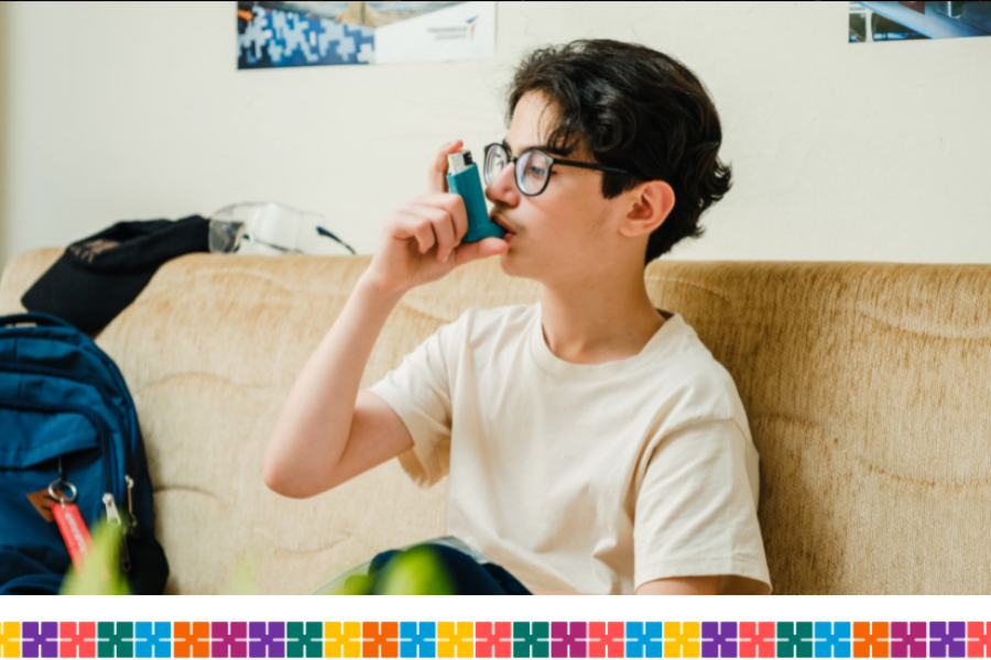 Young boy sitting on a couch using an asthma inhaler.