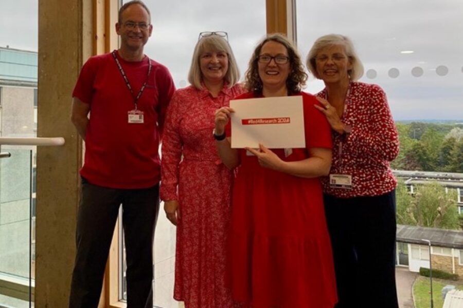 Standing left to right are Dr Phil Smith (co-Head Research and Innovation, HWE ICB), Fiona Smith (co-Head Research and Innovation, HWE ICB), Dr Rebecca Hadley (Senior Research Fellow, University of Hertfordshire) and Dr Lisa Whiting (Associate Dean of Research, University of Hertfordshire) all wearing red. Dr Rebecca Hadley is holding up a piece of paper which says #Red4Research 2024 in big letters