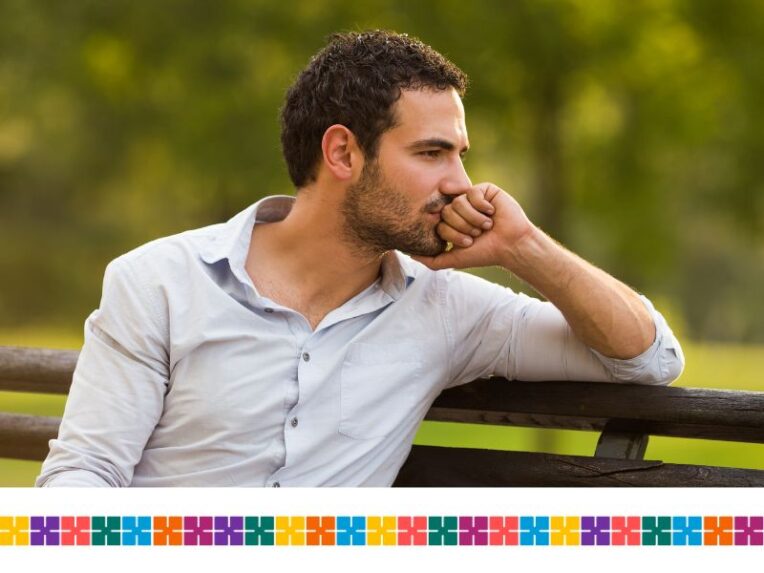 Man looking worried sat on park bench.